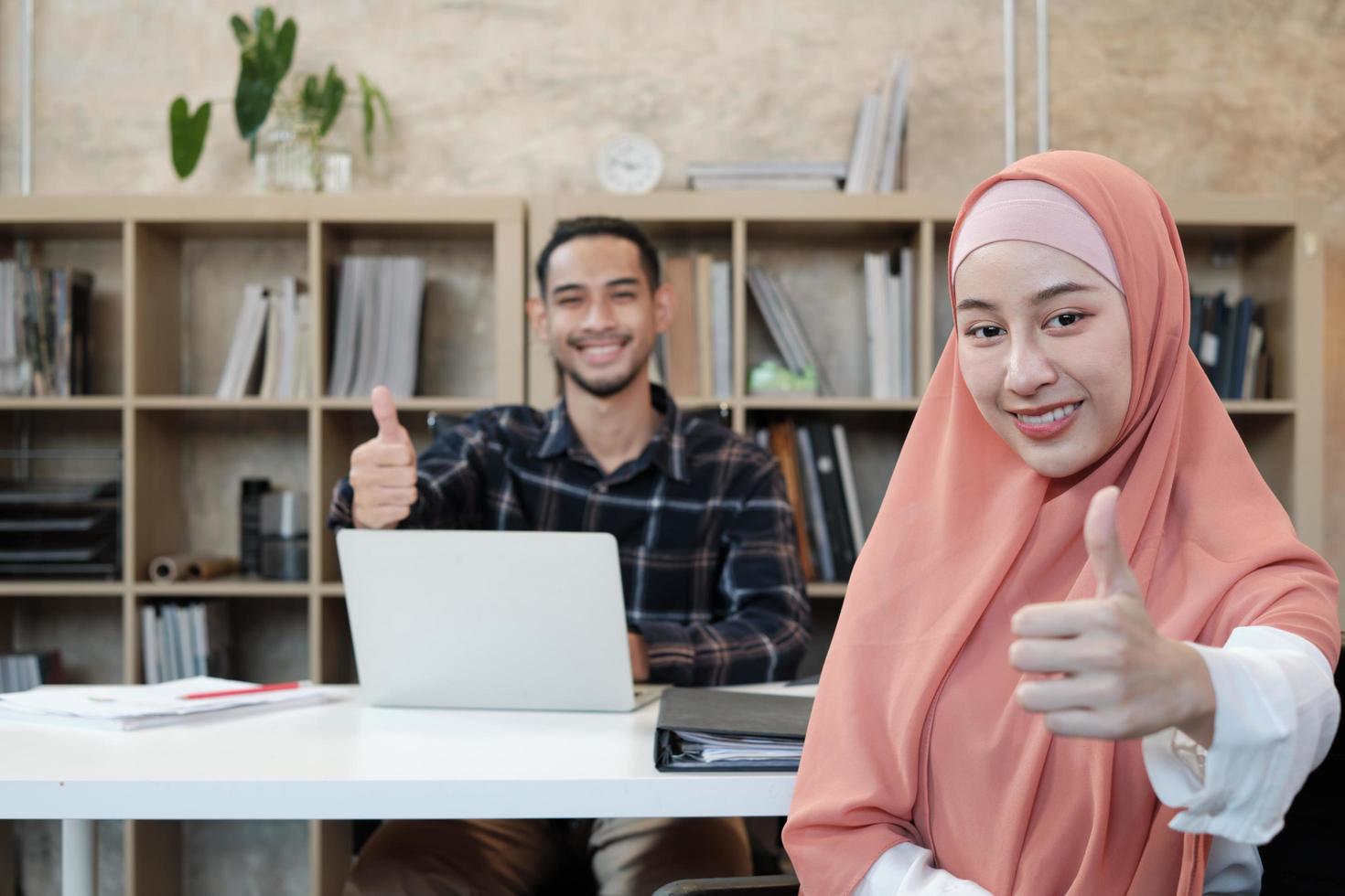 Portrait of entrepreneur of business startup, young male and beautiful female owner, two partners Islamic people, looking at camera, smiles happily and thumb up in small e-commerce workplace office. photo