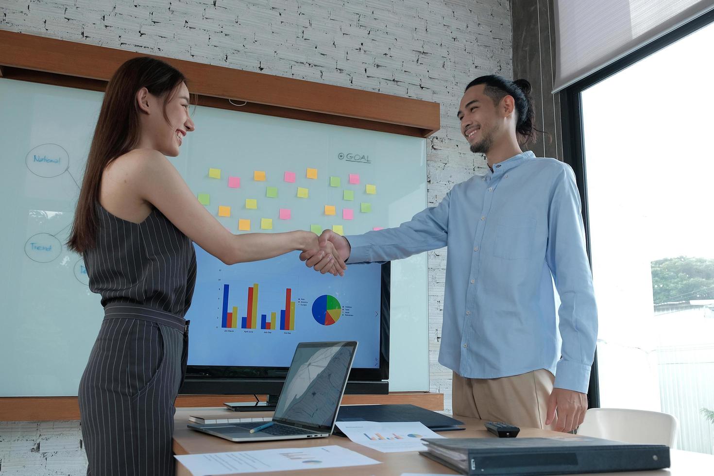 Businesspersons of Asian ethnicity are shaking hands to deal with commercial partnerships and work together after a beautiful young woman manager presents a success chart in the office meeting room. photo