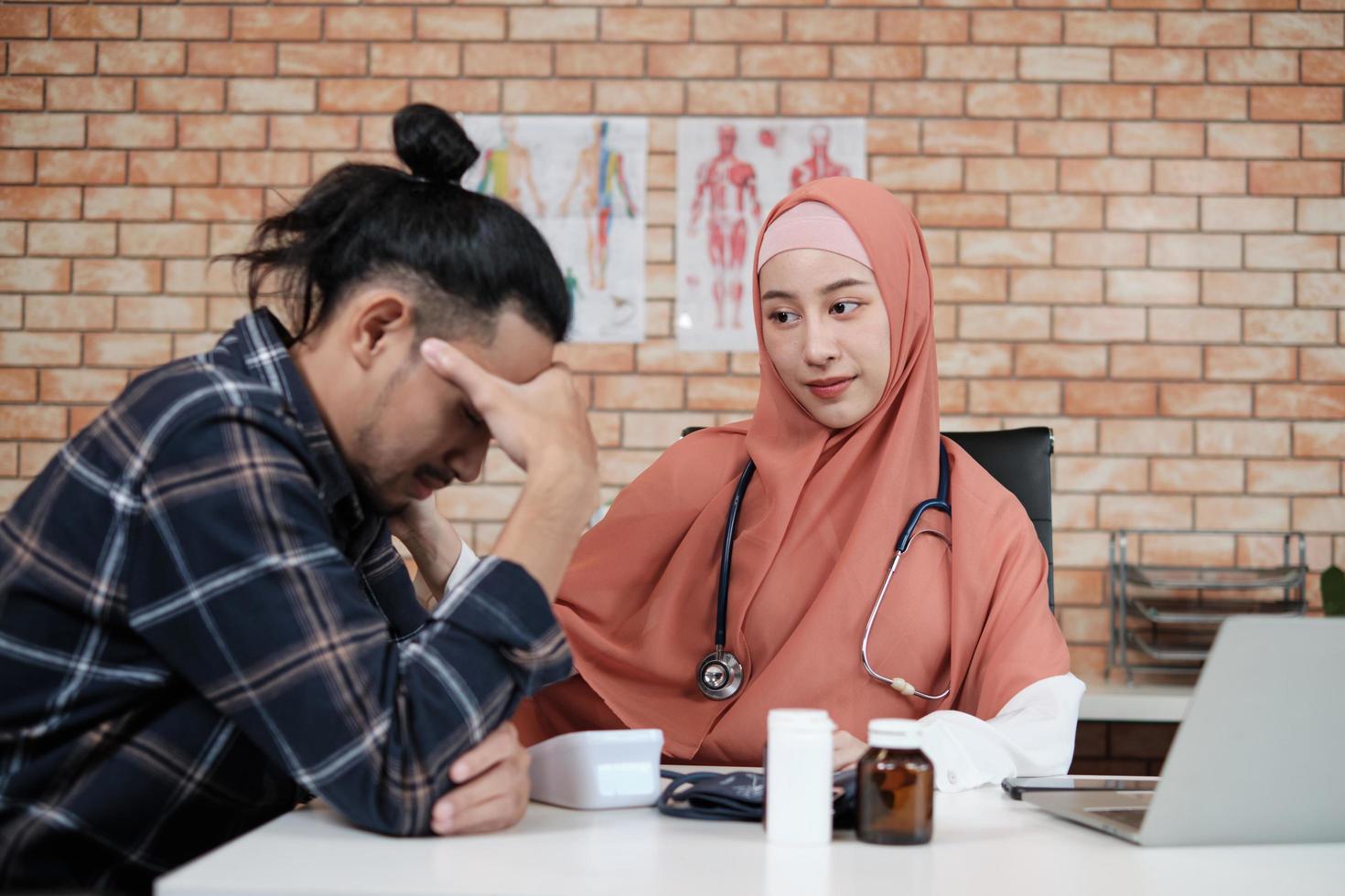 A young beautiful doctor, a person who is female Muslim encourages and comforting male patient of Asian ethnicity who is sad and illness, at health and medical treatment clinic's office in hospital. photo