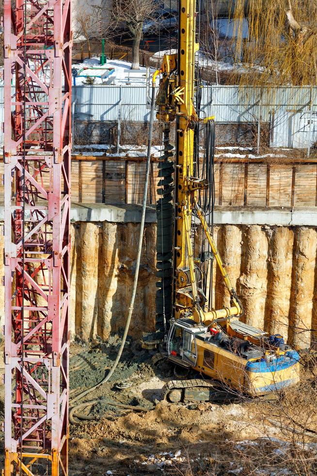 una excavadora pesada, junto con una plataforma de perforación, está trabajando en un sitio de construcción para fortalecer los cimientos de un futuro rascacielos. imagen vertical. foto