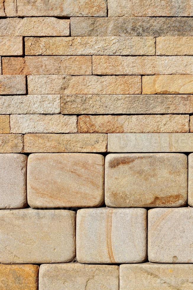 A stack of hewn, rounded yellow sandstone stones in the lower half and rough rectangular tiles at the top. photo