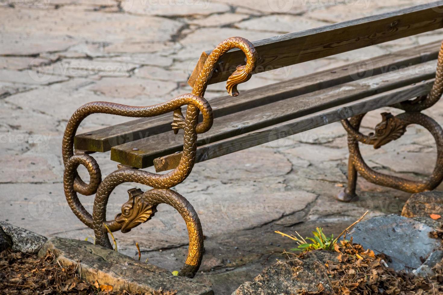 banco en el parque al atardecer con barandilla de metal en forma de serpiente o dragón en austria. foto