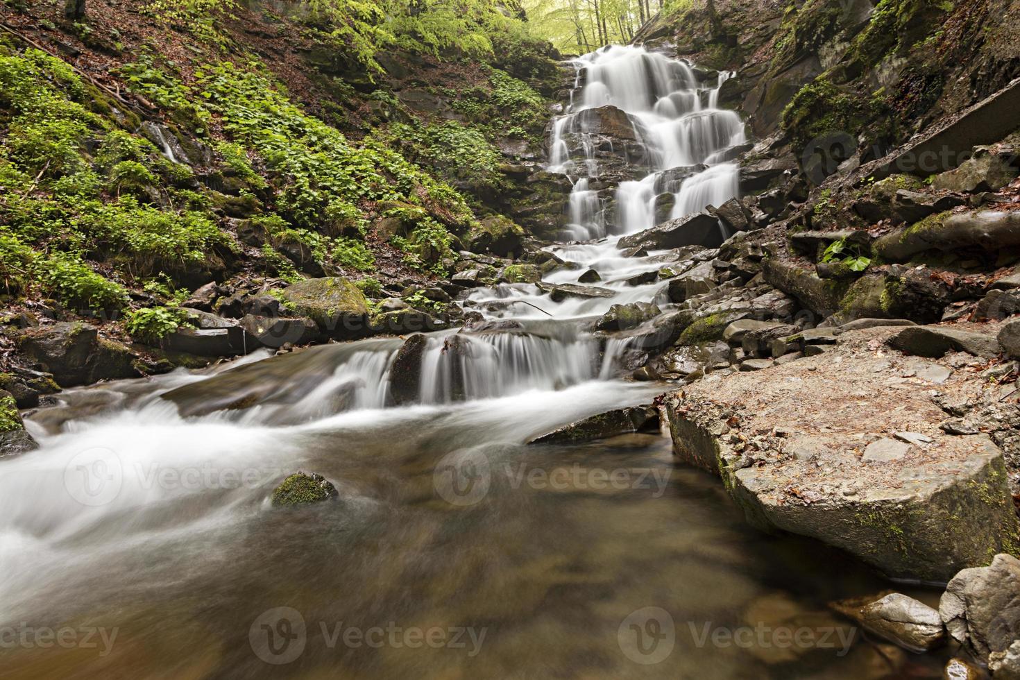 A large boulder lies at the foot of a waterfall in the Carpathian mountains photo