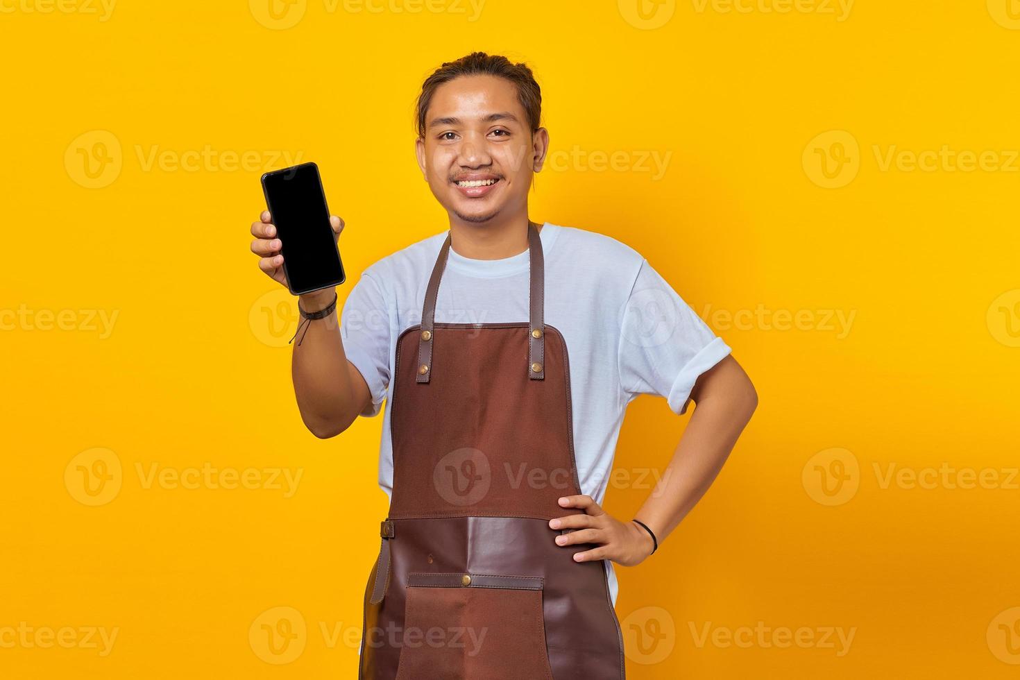 Excited Asian barista showing smartphone blank screen over yellow background photo