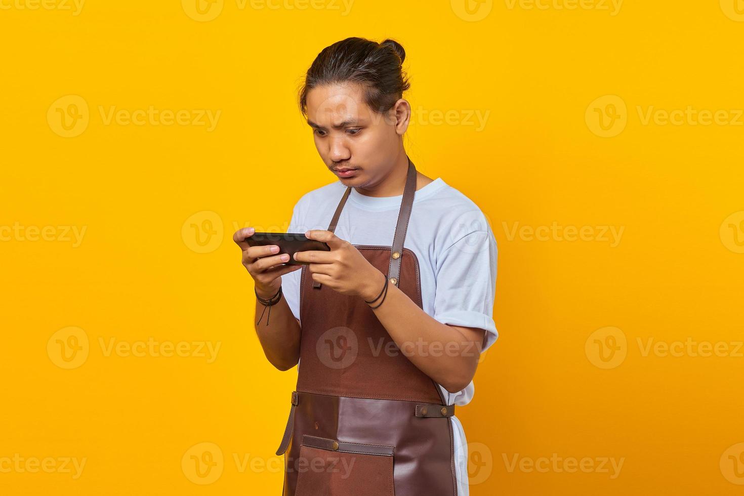 Attractive young asian barista using mobile phone playing game on yellow background photo