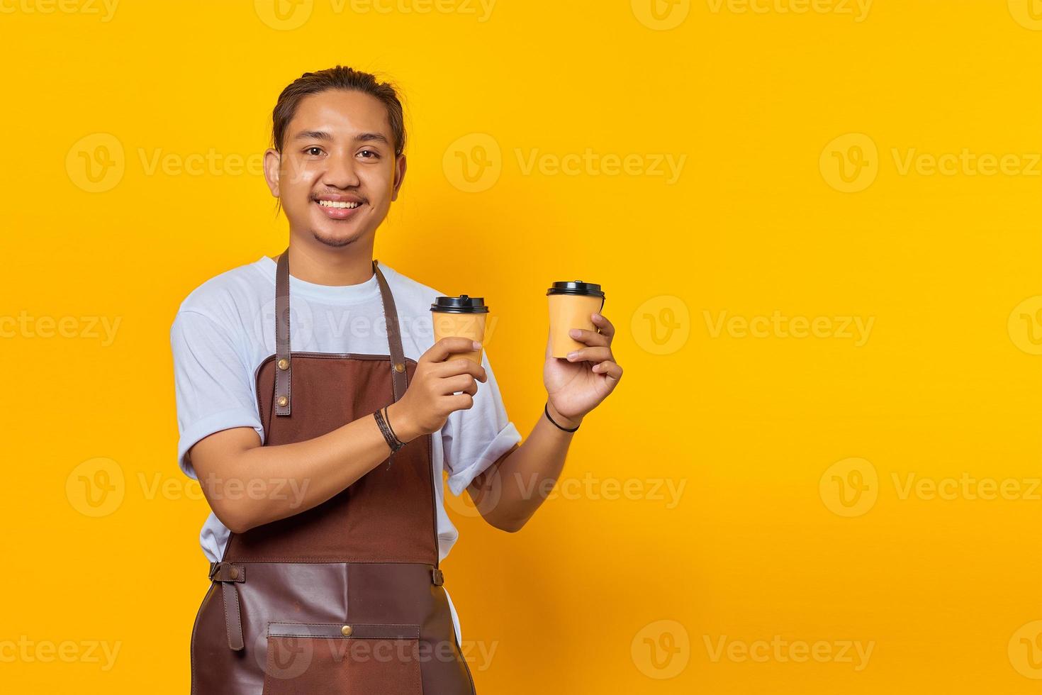 Portrait of cheerful barista man holding two paper coffee cups for you to choose isolated on yellow background photo