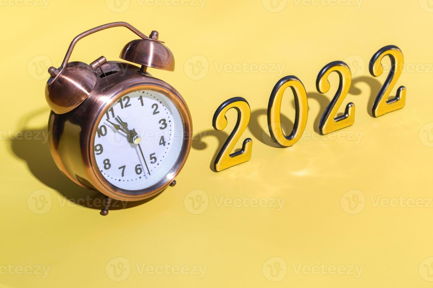 Alarm clock and numbers 2022 with hard shadow on yellow background. New year celebration minimal concept. Close up. copy space photo