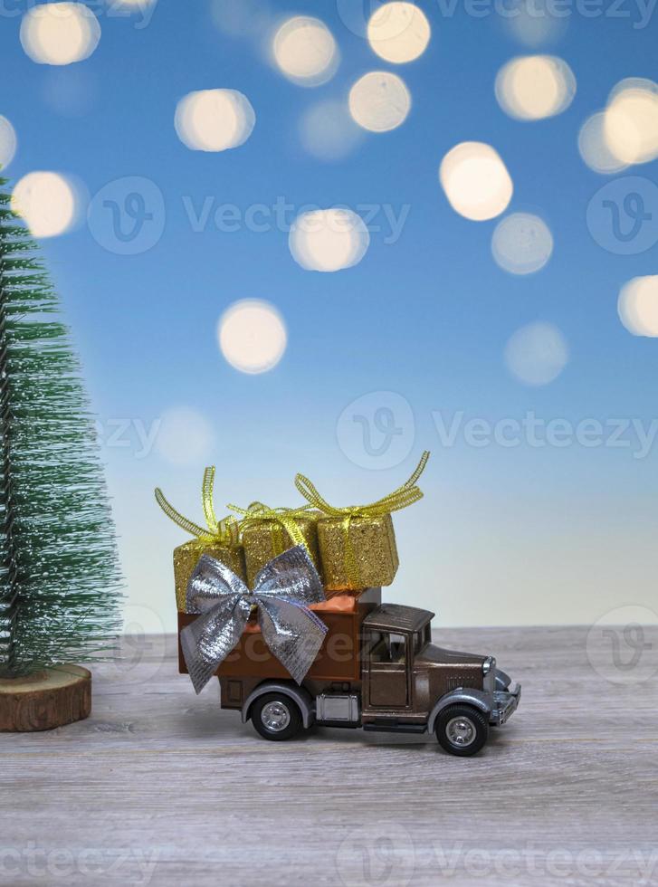 Retro Santa's truck with Christmas gifts on the background of a Christmas tree and blue sky in lights. Close up with copy space. Vertical photo