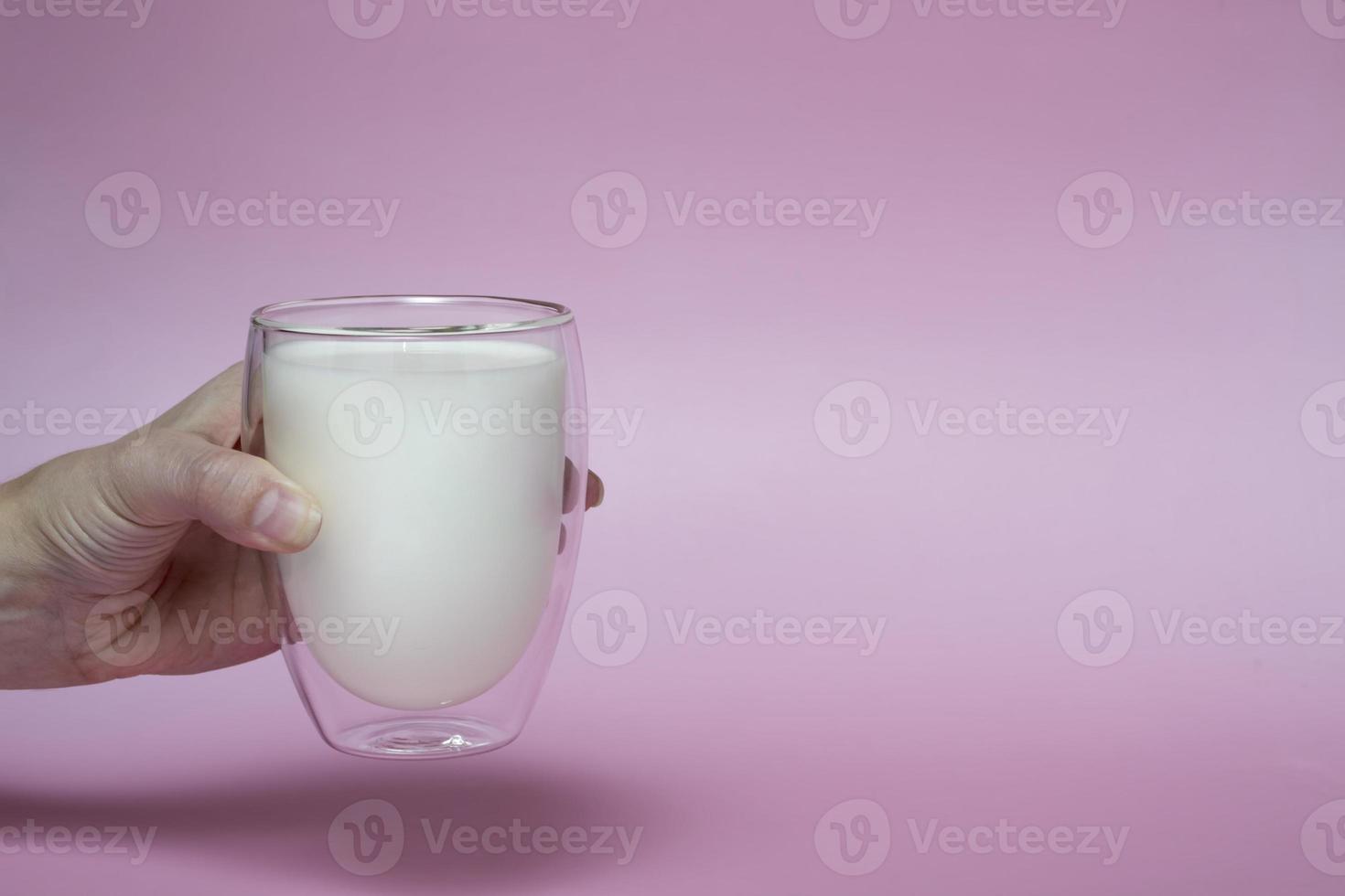 female hand holding a glass with fresh milk, on a pink background,fortified drink, calcium photo