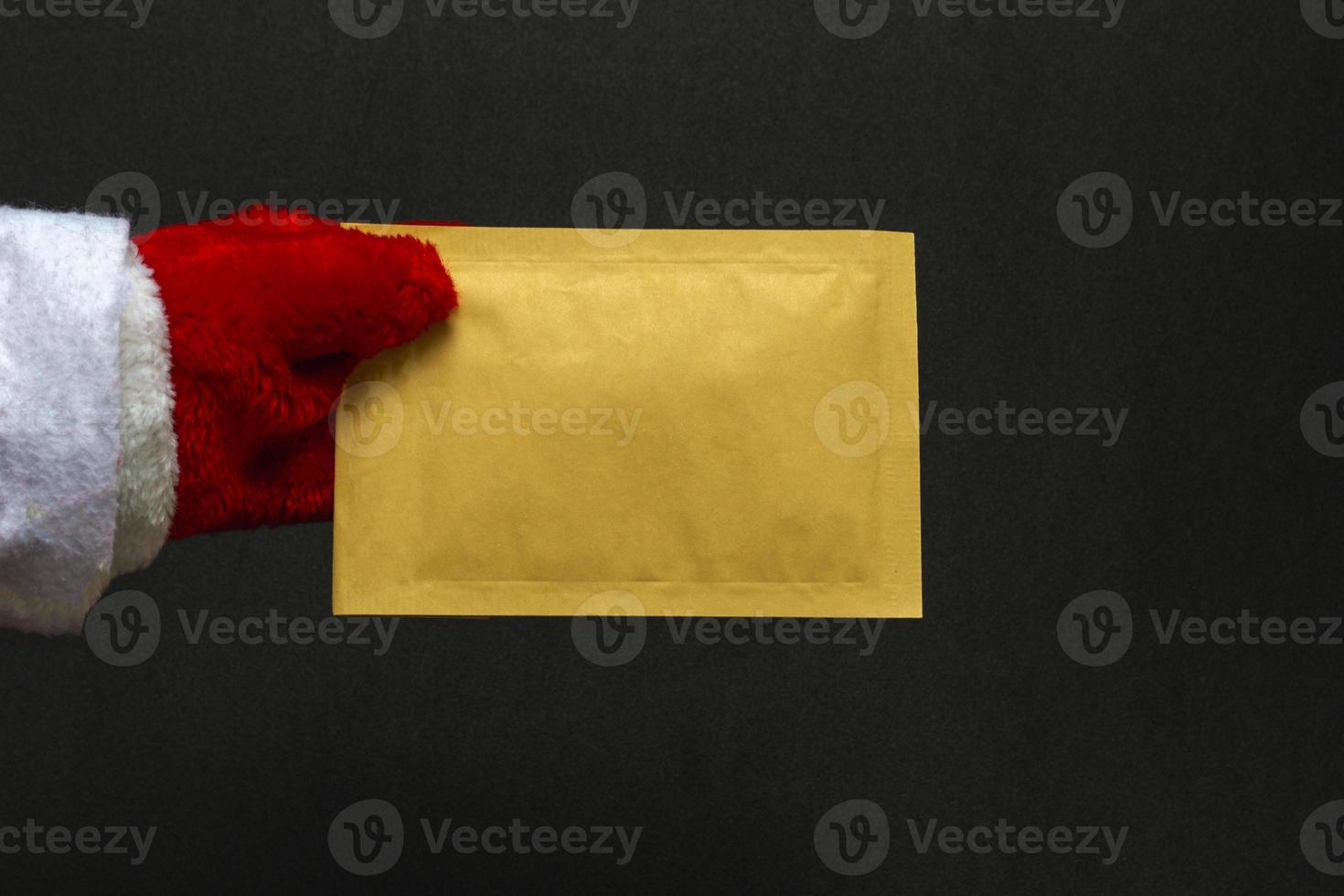 Merry Christmas and Happy New Year concept. Close up on black background santa claus hand holding envelope, copy space photo