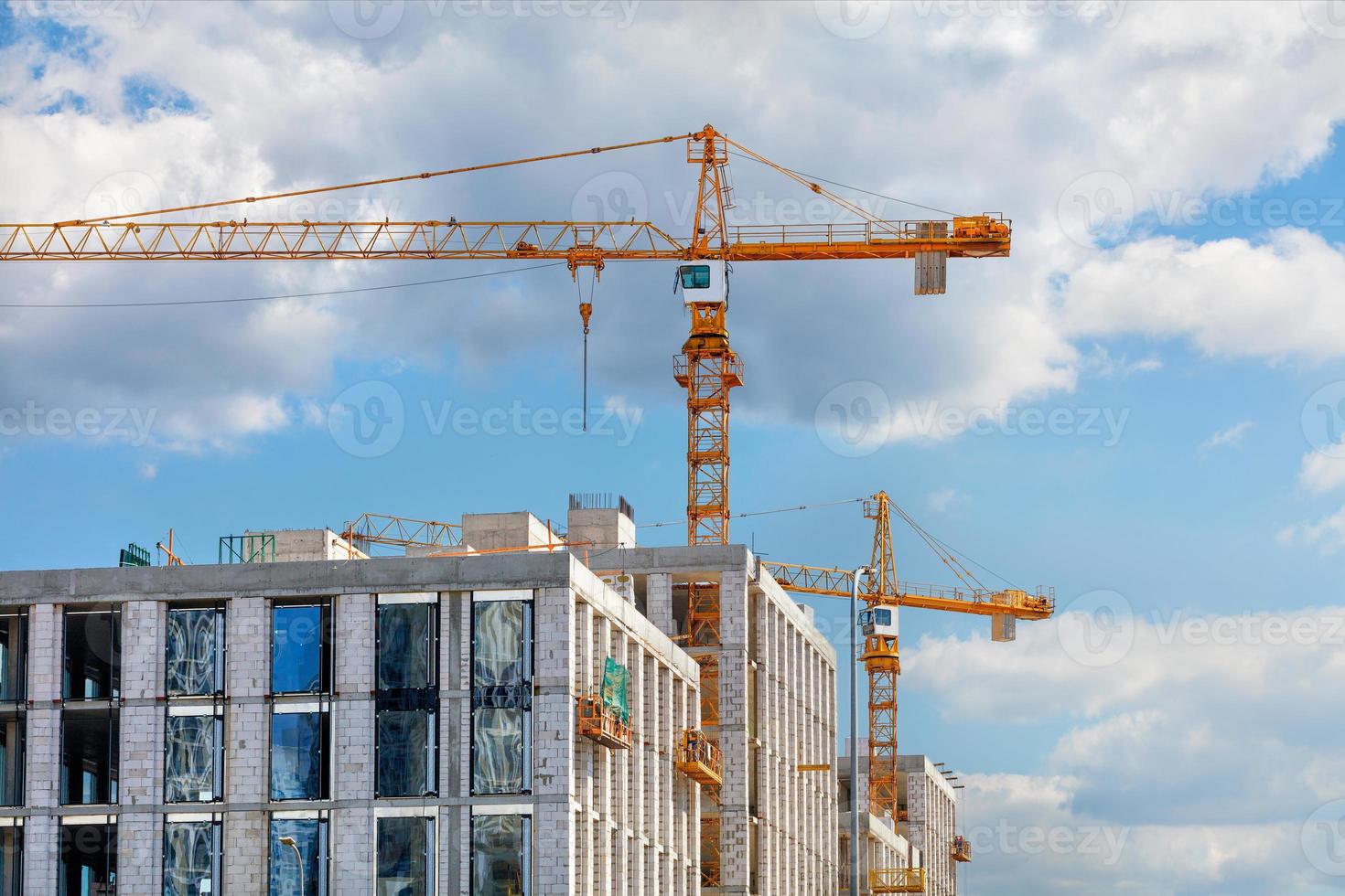 Construcción de un edificio residencial de varios pisos con grúas torre contra un cielo azul ligeramente nublado. foto