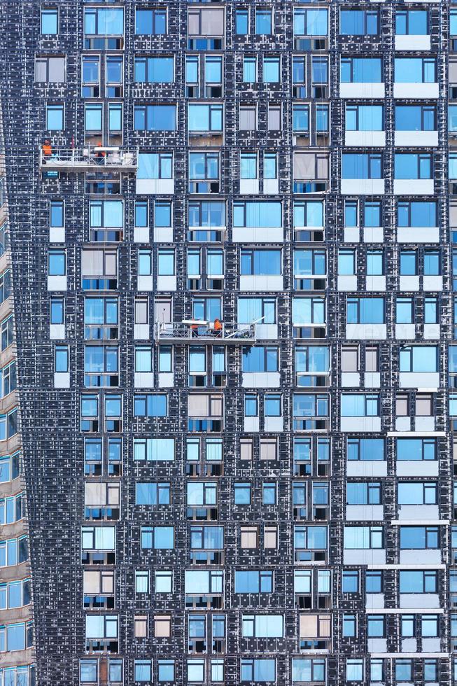 fragmento de la fachada de un edificio de gran altura en construcción y su aislamiento mediante cabrestantes y plataformas móviles, el concepto de ahorro energético en la construcción residencial. foto