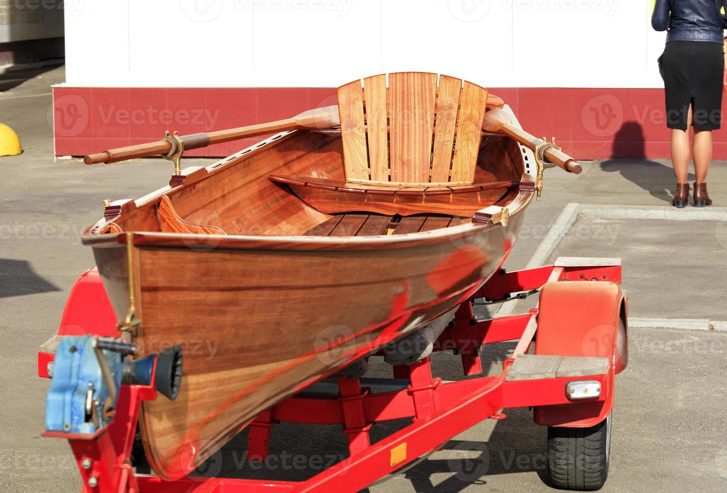 An orange wooden canoe rests in a car park. photo