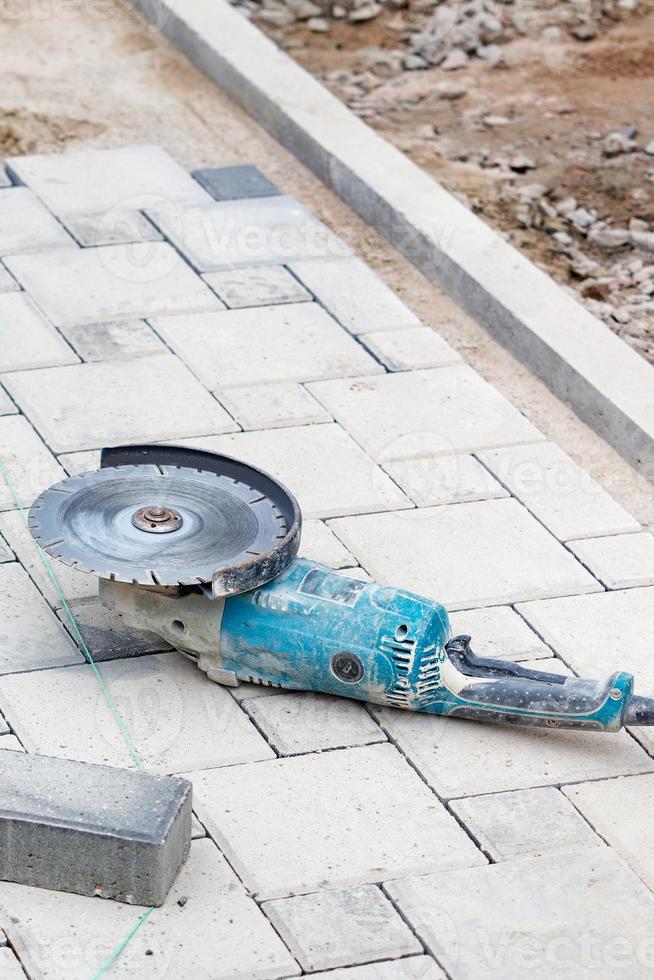 A worn-out angle grinder with diamond discs lies on paving slabs in front of the workplace. Vertical image, copy space. photo