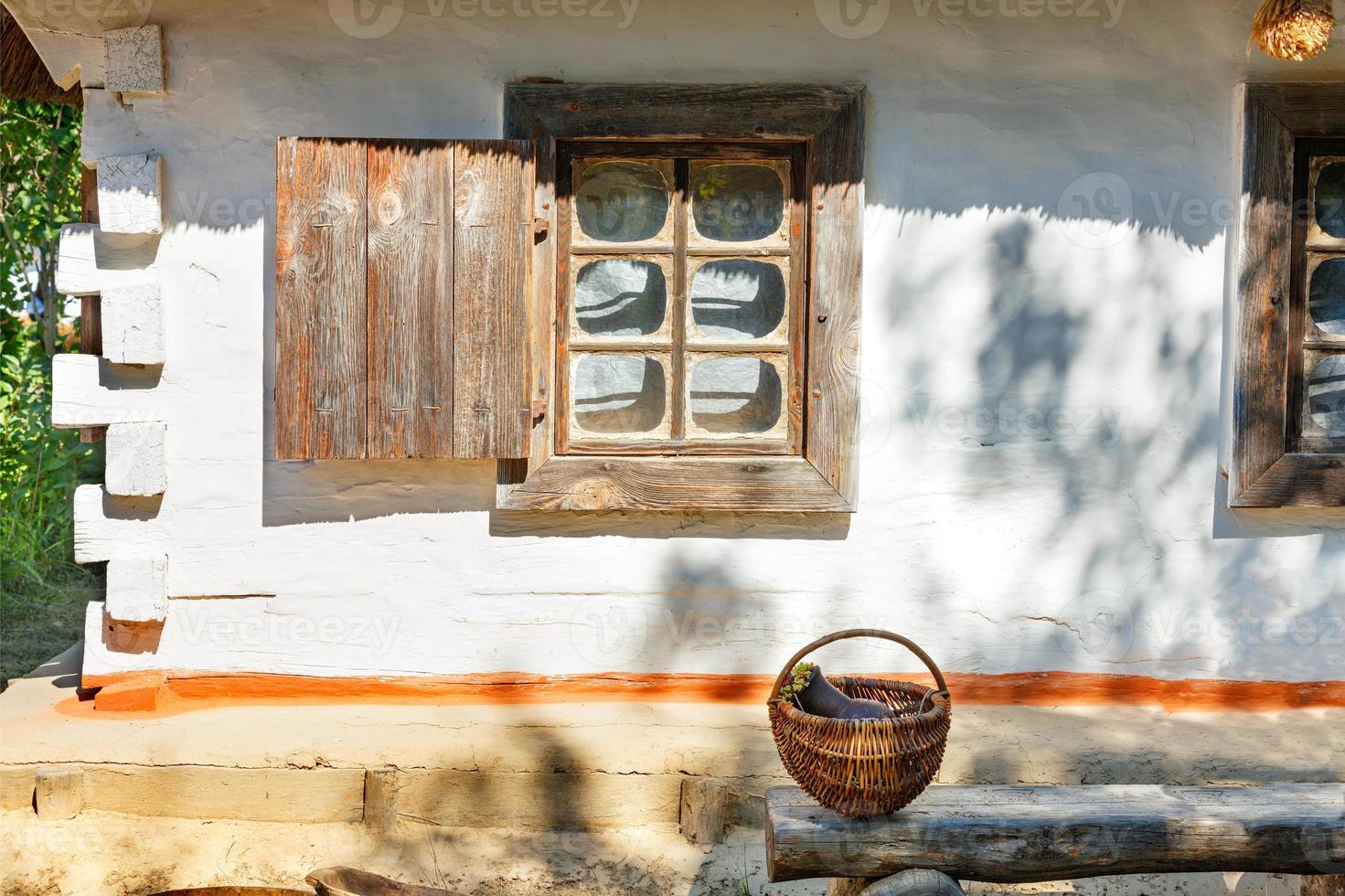 una vieja ventana con contraventanas de madera de una cabaña rural ucraniana bajo un techo de paja está iluminada por los rayos del sol. foto