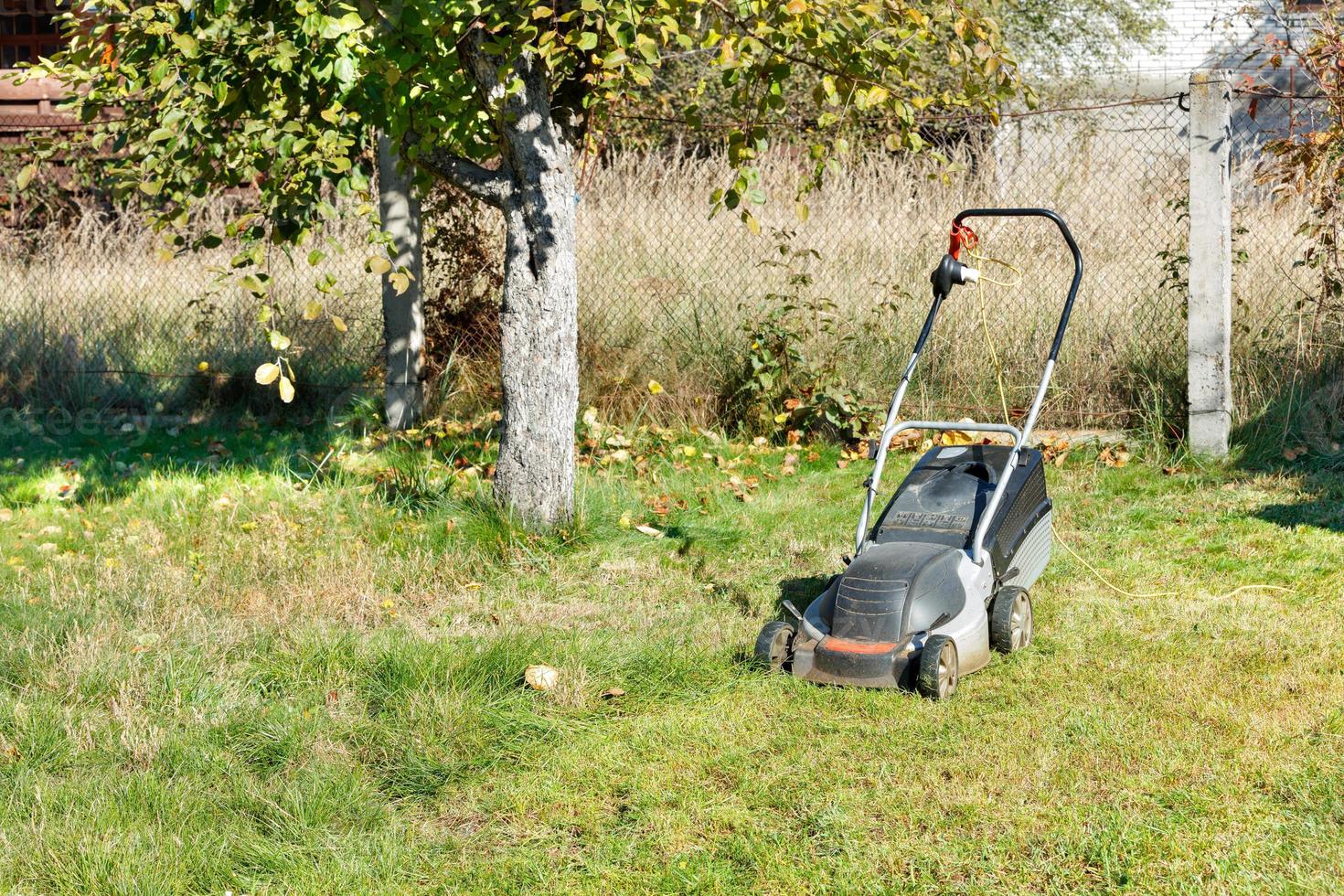 An electric lawn mower stands on a green lawn in a garden area in bright sunlight. photo