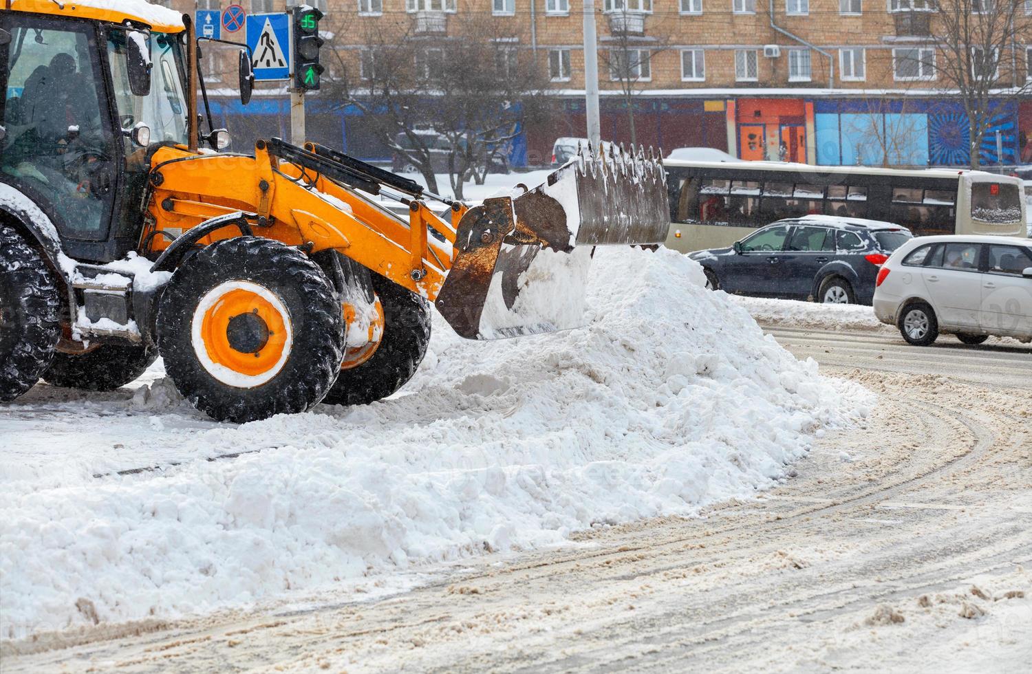 A large ladle of a yellow bulldozer shovels snow from a city road during a snowfall. photo