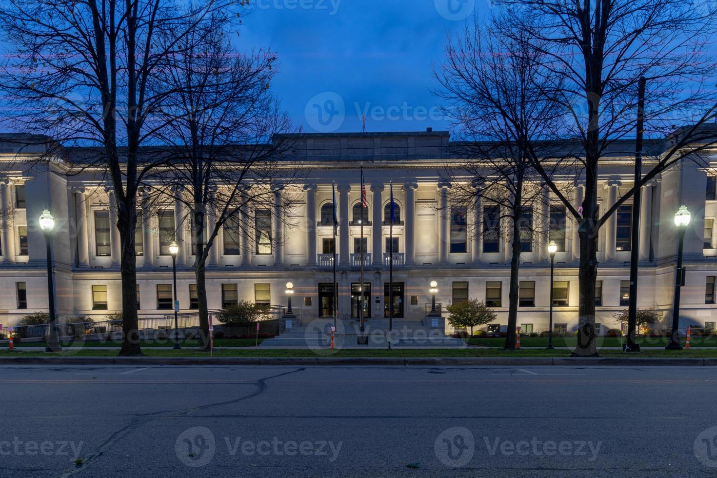 Kenosha County Courthouse, Wisconsin,  illuminated at night.   Tall majestic bare trees lining the entry.   Large steps leading to entry. photo