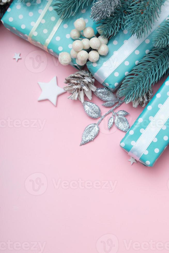 Tarjeta de felicitación de Navidad con regalos azules, bayas y pino plano sentar sobre fondo rosa con formato vertical de espacio de copia foto