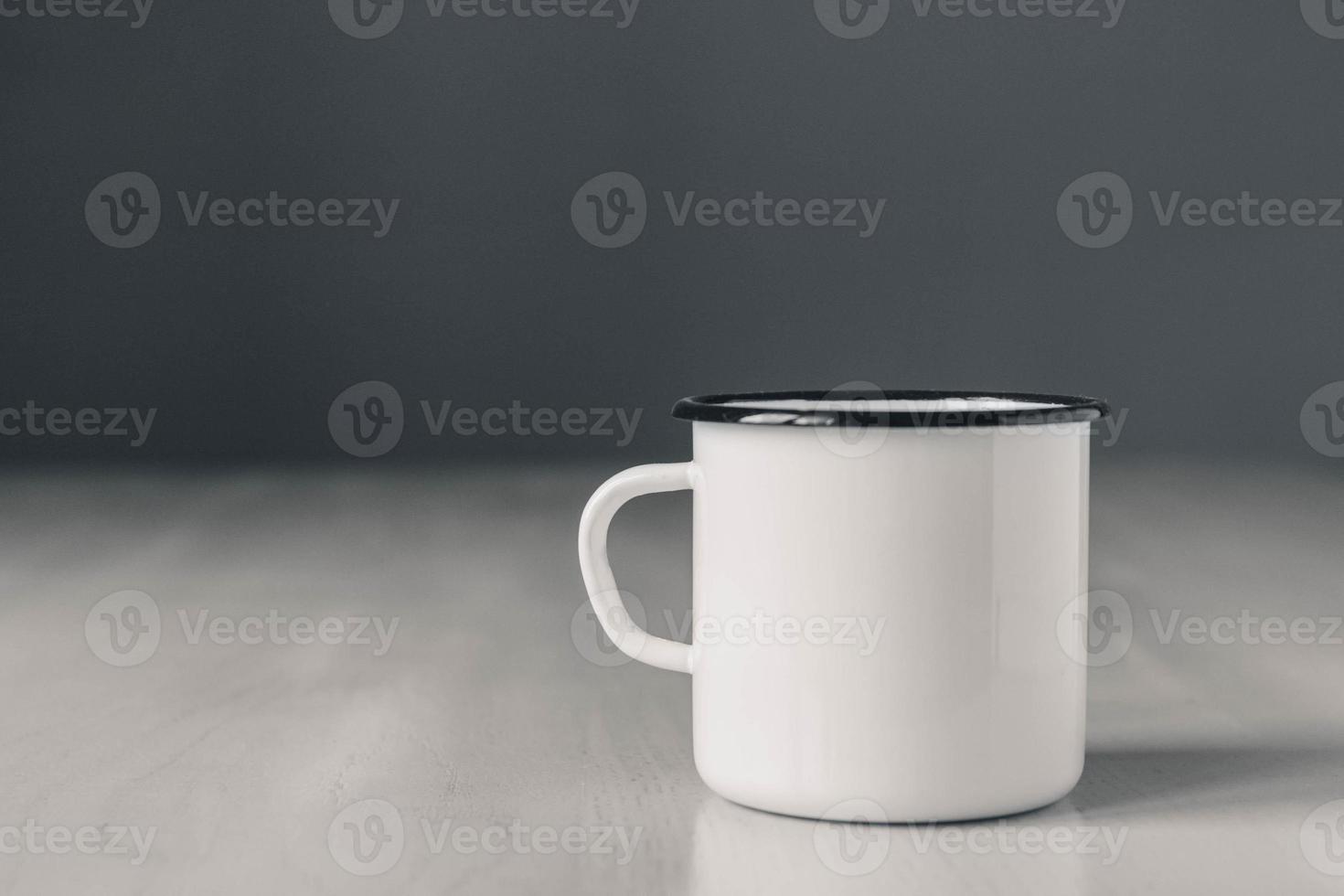 Enamel white metal mug with black line on edge on white wooden table photo