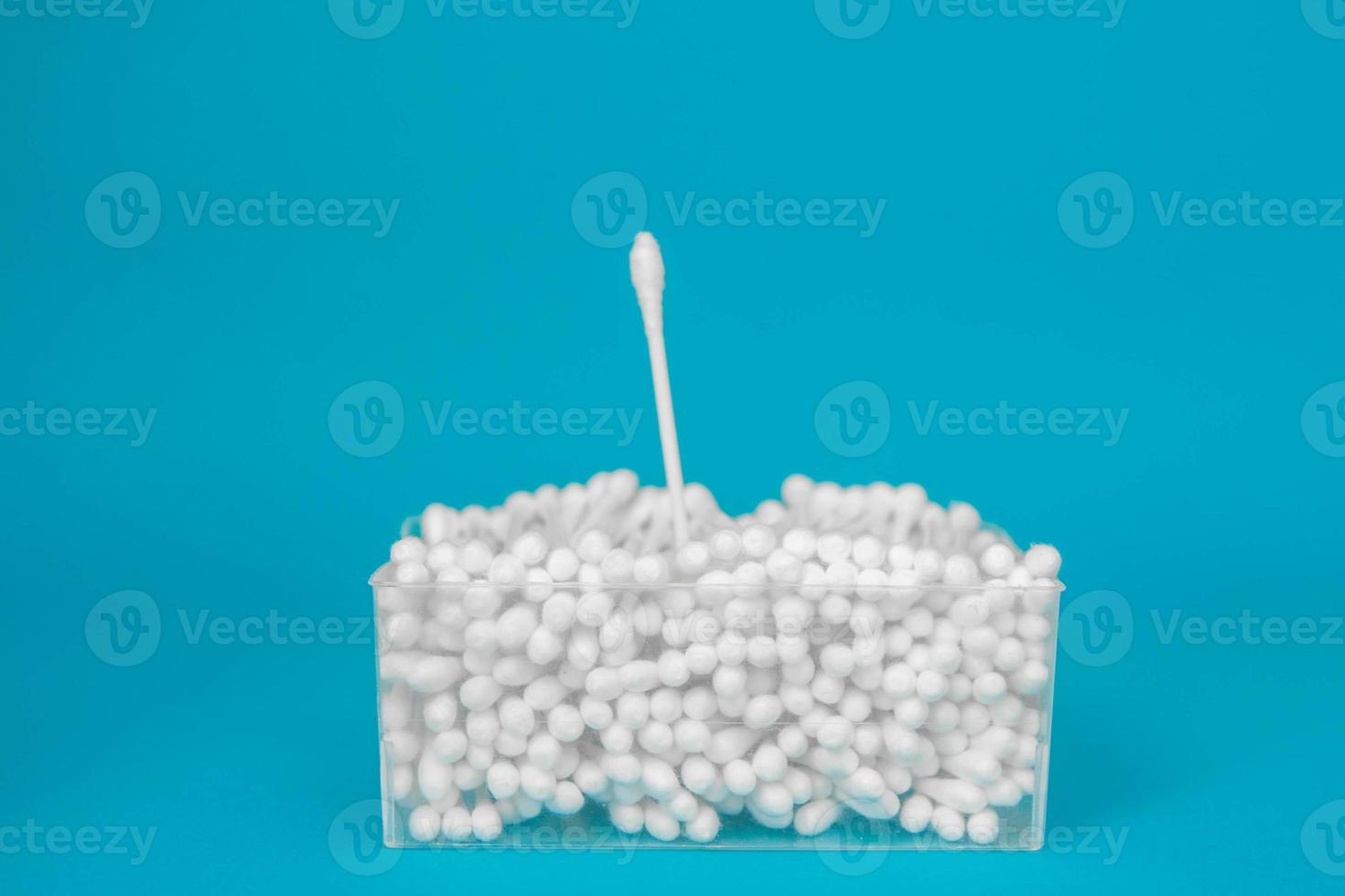 Cotton buds in plastic transparent rectangular container and several cotton buds separately on a blue background photo