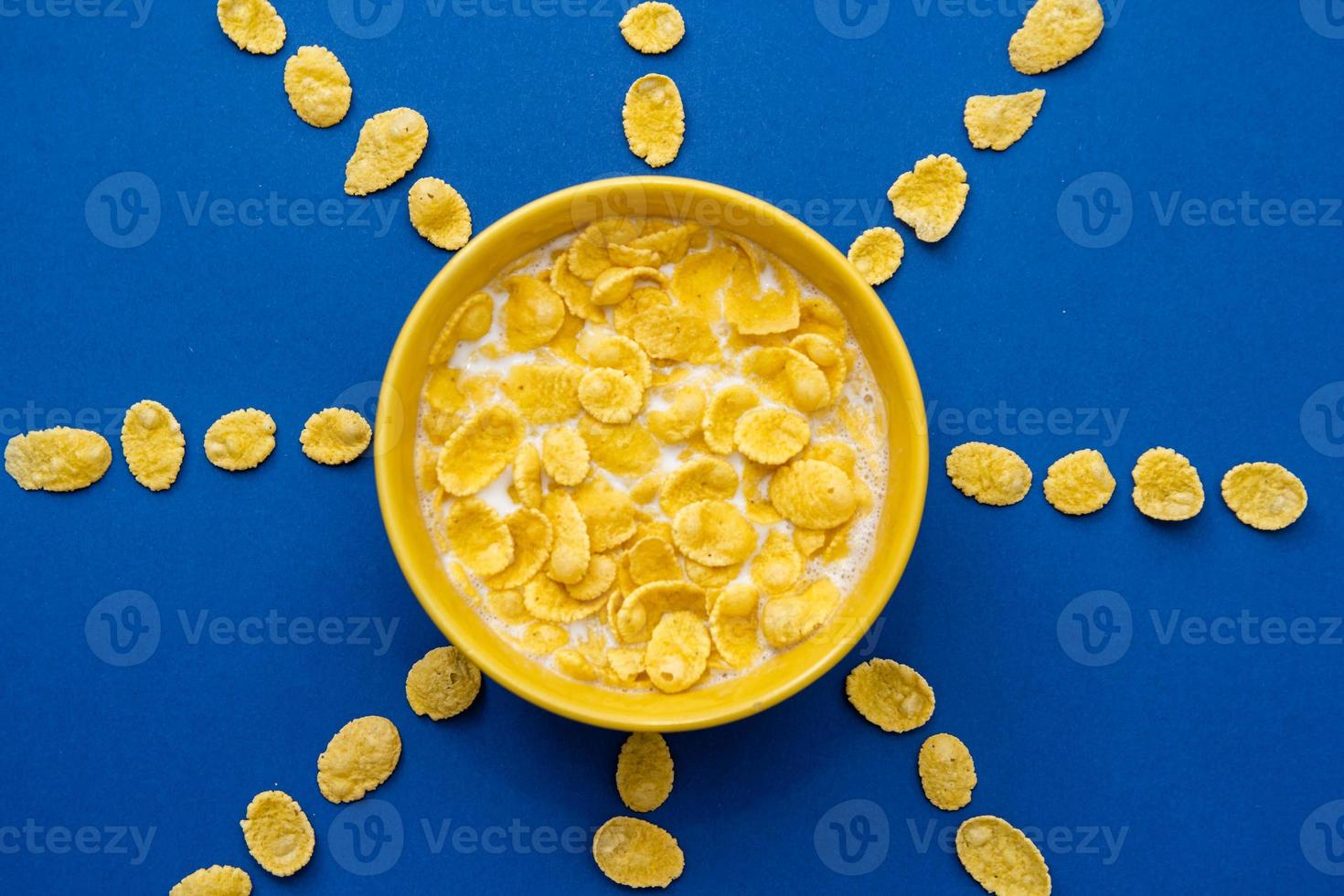 Copos de maíz con leche en el recipiente amarillo en forma de sol sobre fondo azul. foto