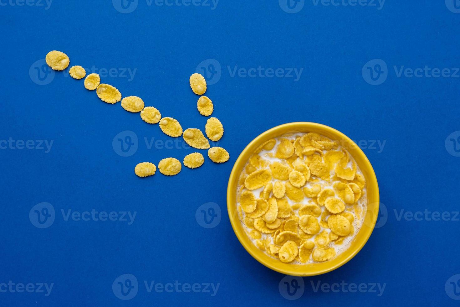 Copos de maíz con leche en el recipiente amarillo sobre fondo azul. foto