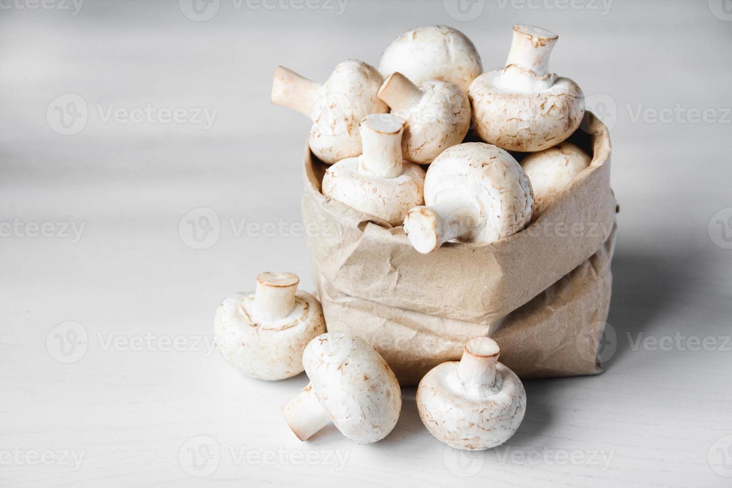 Champiñones champiñones en una bolsa de papel sobre una mesa de madera blanca foto