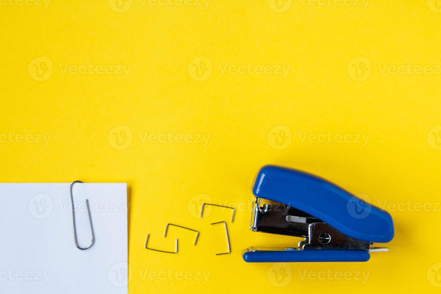 Blue stapler with metal staples and paper clip on yellow background photo