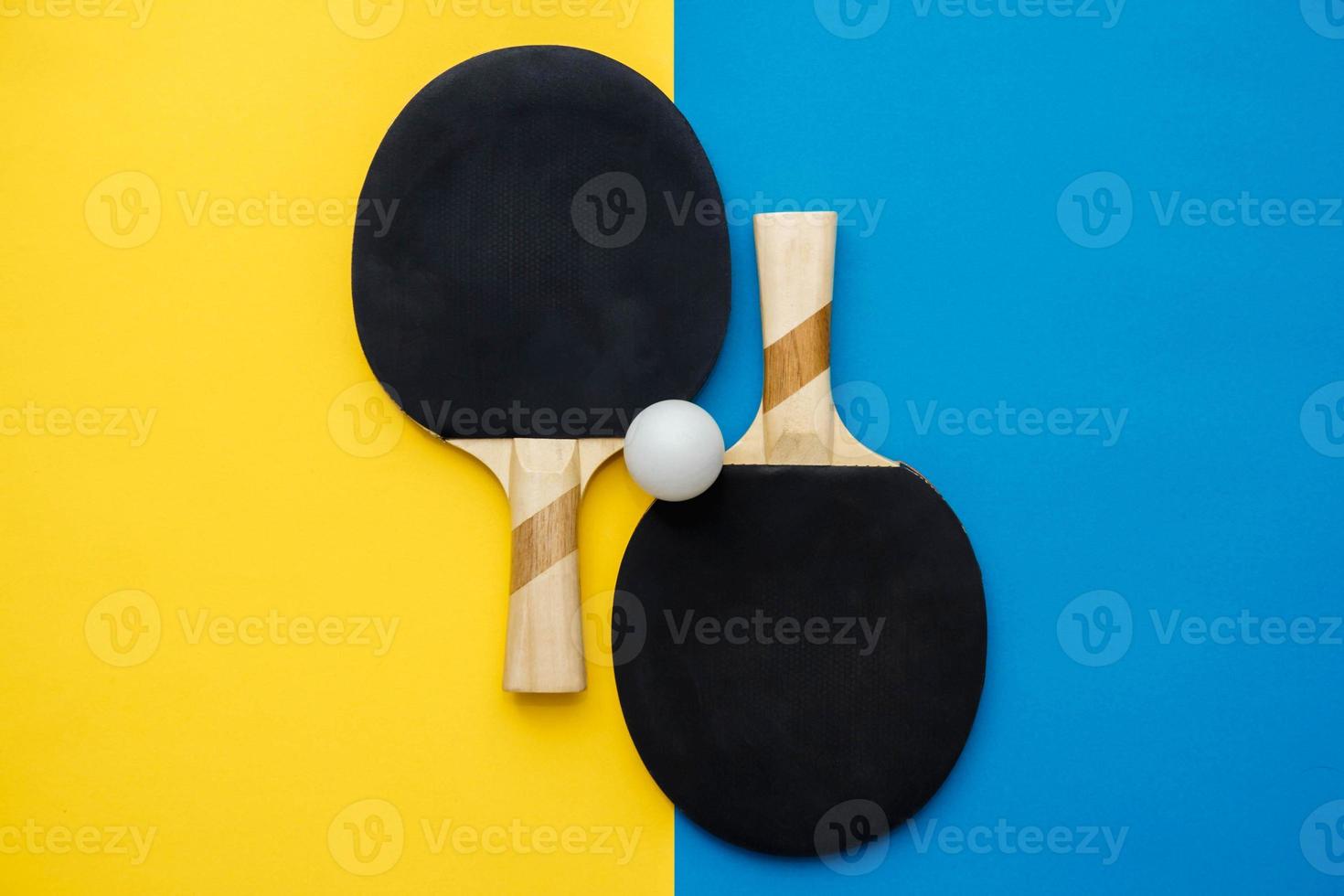 Two table tennis or ping pong rackets and ball on blue and yellow background photo