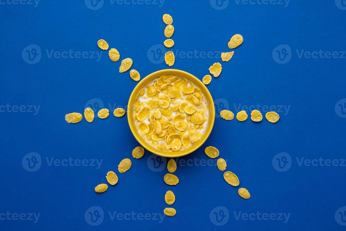 Copos de maíz con leche en el recipiente amarillo en forma de sol sobre fondo azul. foto