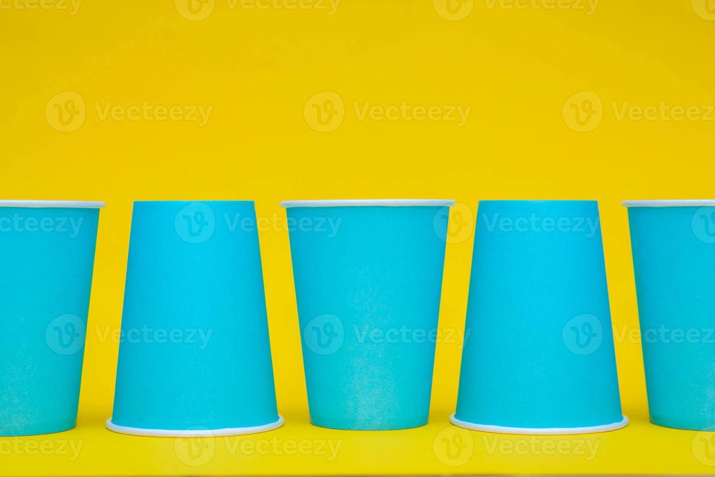 Colocación de vasos de papel azul en una línea sobre fondo amarillo foto