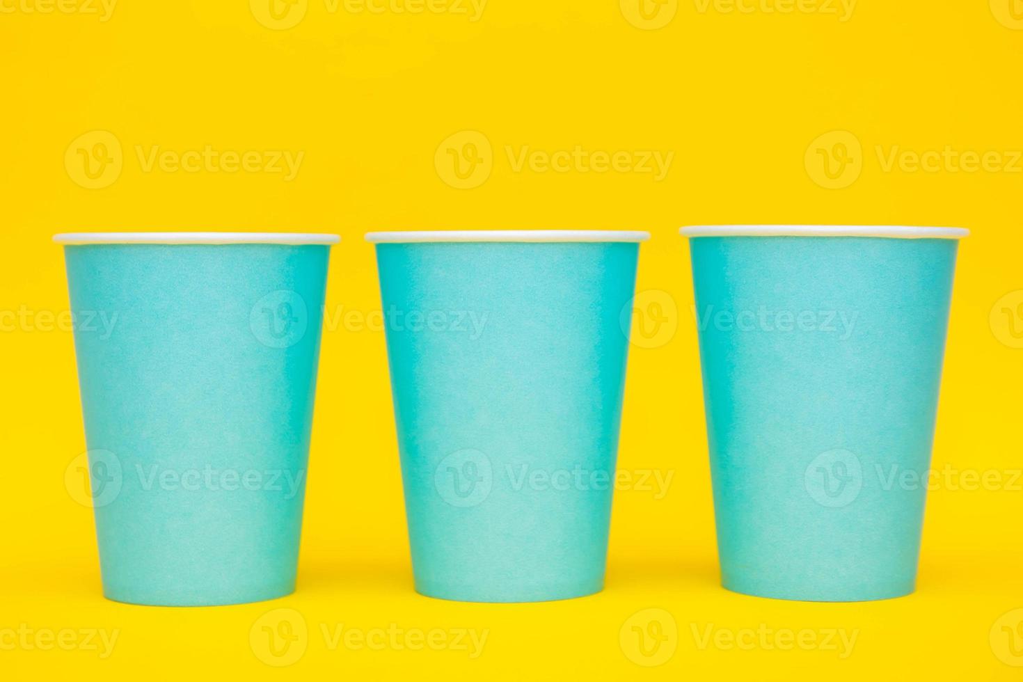 Blue paper cups placement in a line on yellow background photo