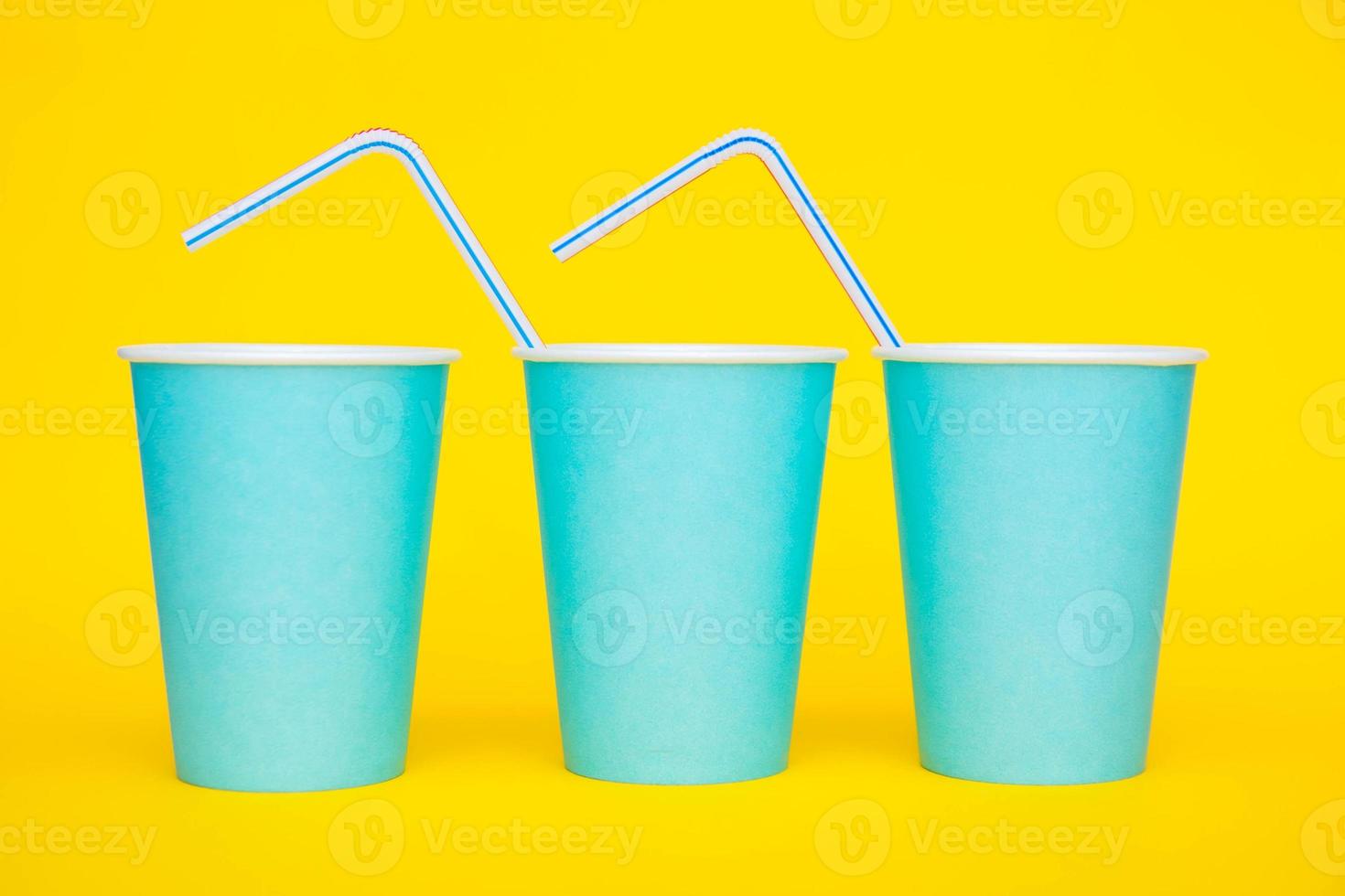 Colocación de vasos de papel azul en una línea con pajitas de plástico de colores para beber sobre fondo amarillo foto