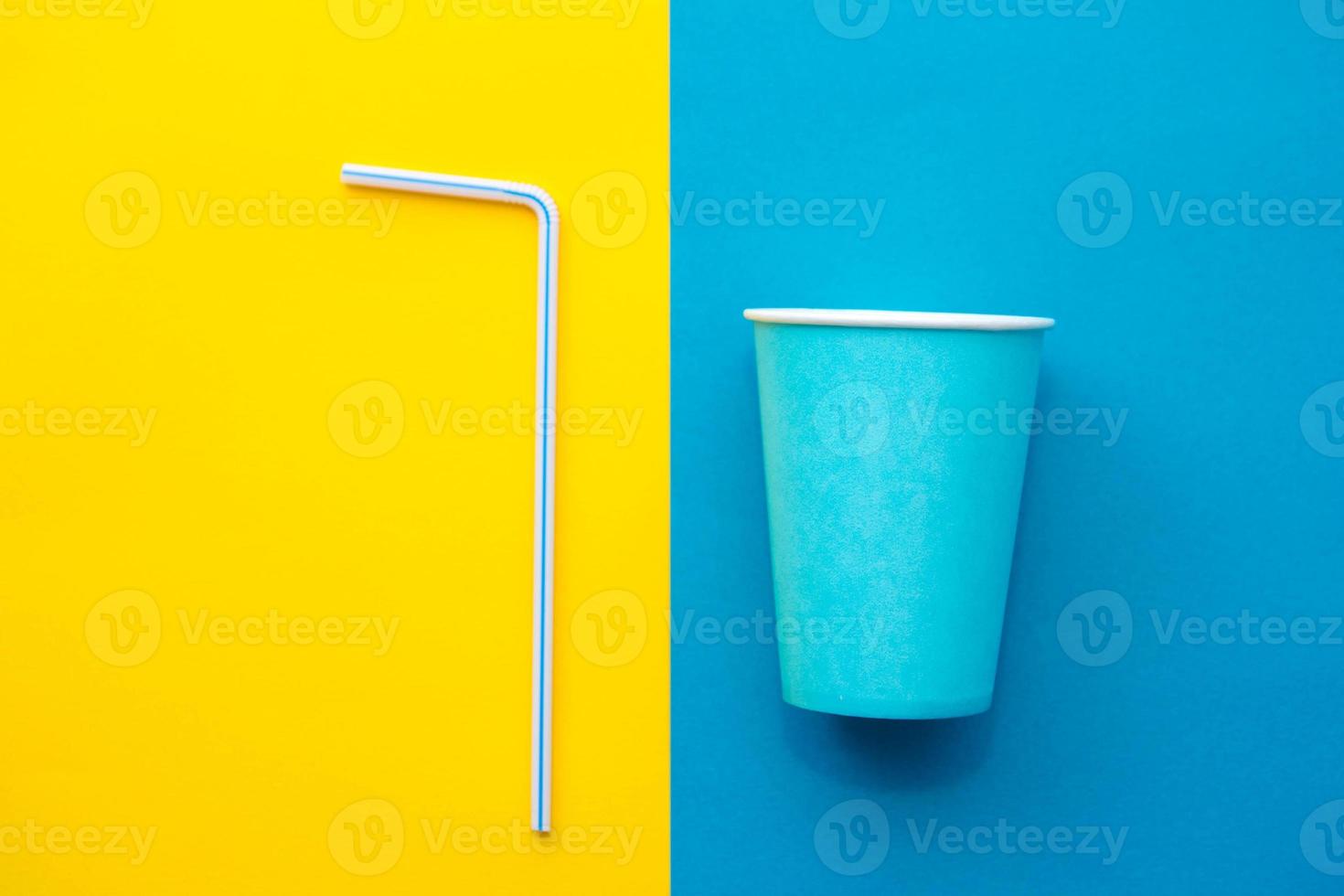 Vasos de papel azul con pajitas de plástico de colores para beber sobre fondo amarillo y azul foto