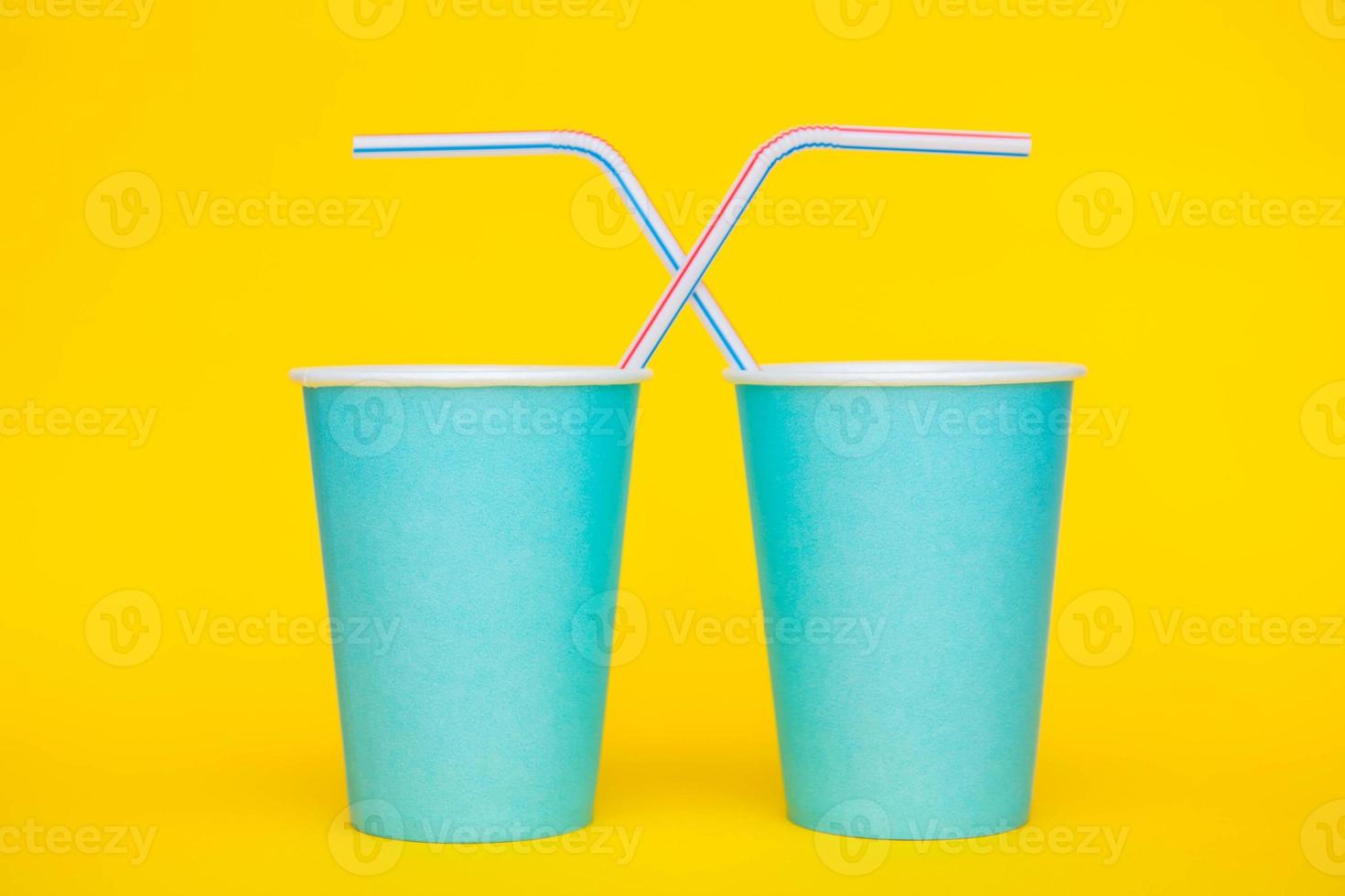 Dos vasos de papel azul con pajitas de plástico de colores para beber sobre fondo amarillo foto