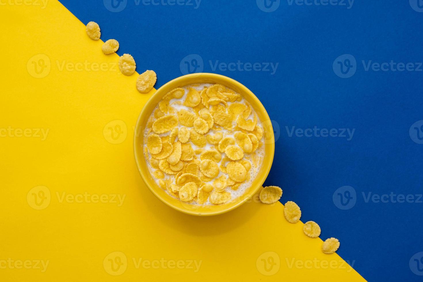 Copos de maíz con leche en el recipiente amarillo sobre fondo azul y amarillo foto