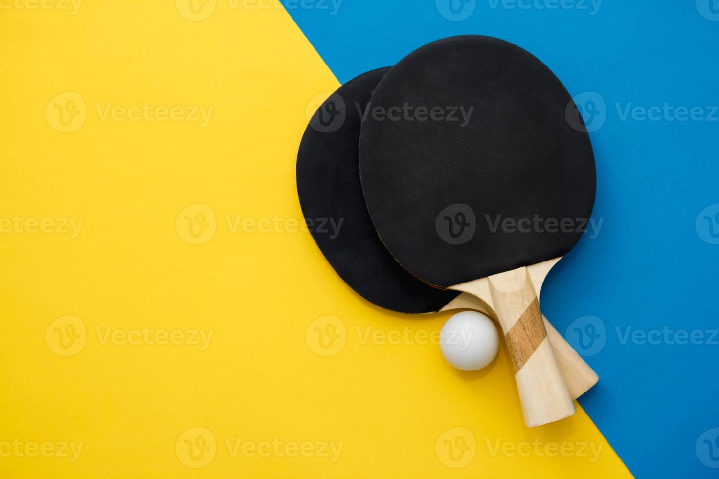 Dos raquetas de tenis de mesa o ping pong y pelota sobre fondo azul y amarillo foto