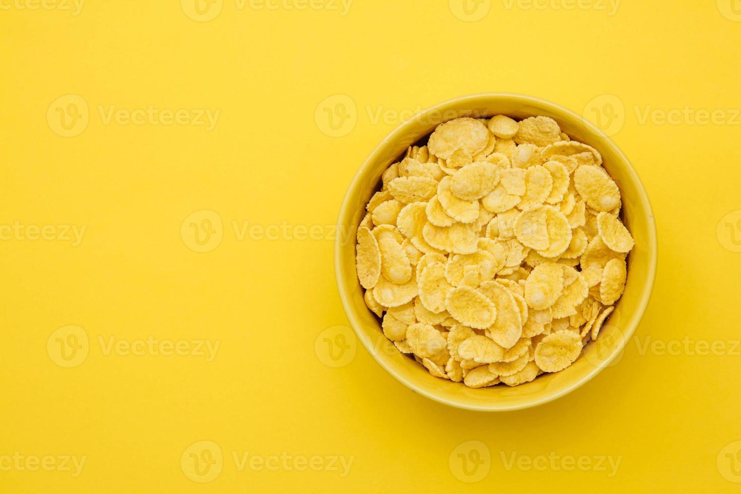 Copos de maíz en un tazón amarillo sobre fondo amarillo para cereales alimentos saludables foto