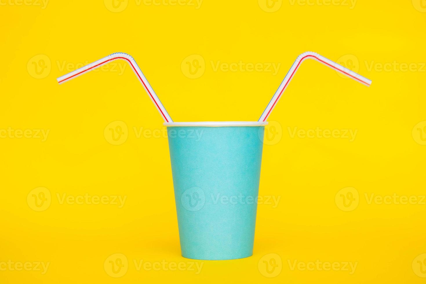 Vaso de papel azul con pajitas de plástico de colores para beber sobre fondo amarillo foto