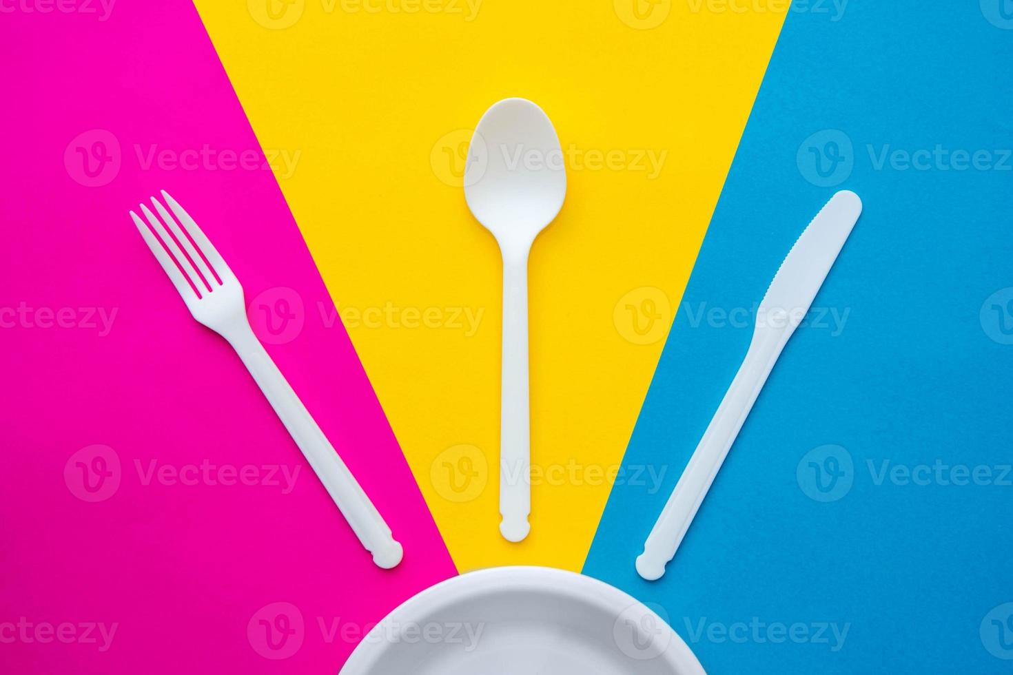 Plastic white fork, knife, spoon and plate on multicolored background photo