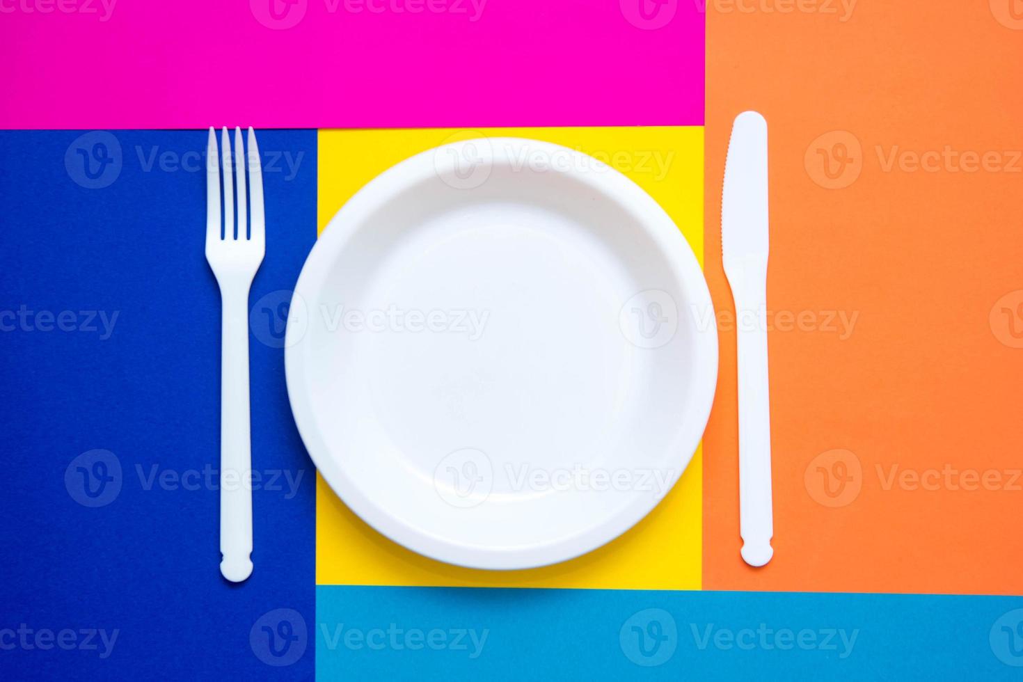 Plastic white fork, knife and plate on multicolored background photo