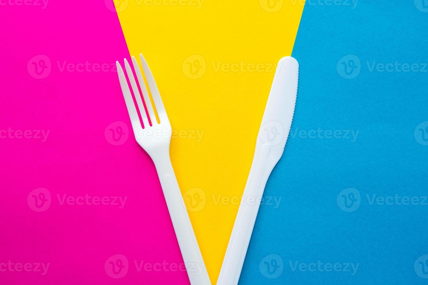 Plastic white fork and knife on multicolored background photo