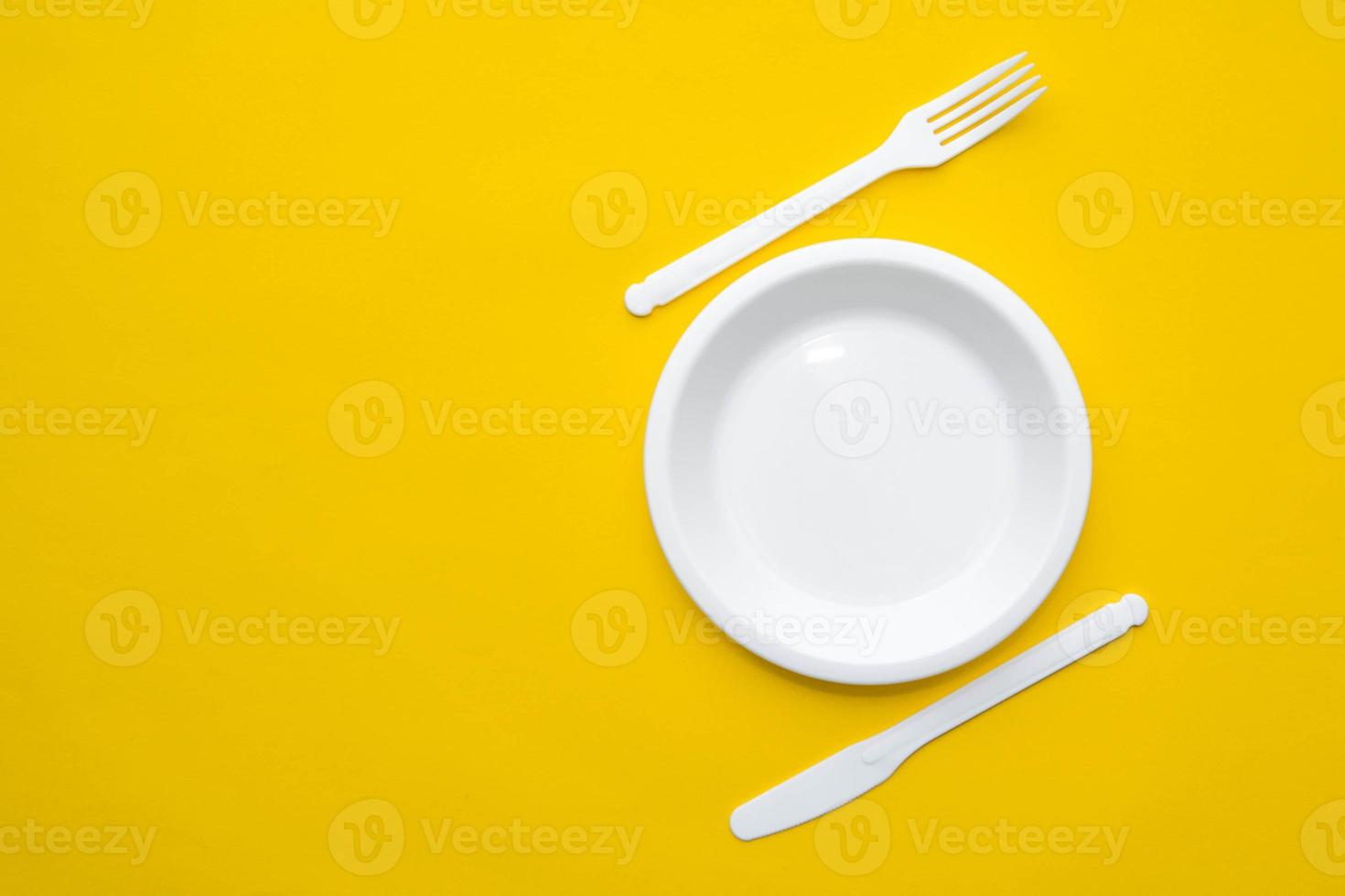 tenedor, cuchillo y plato de plástico blanco sobre fondo amarillo foto