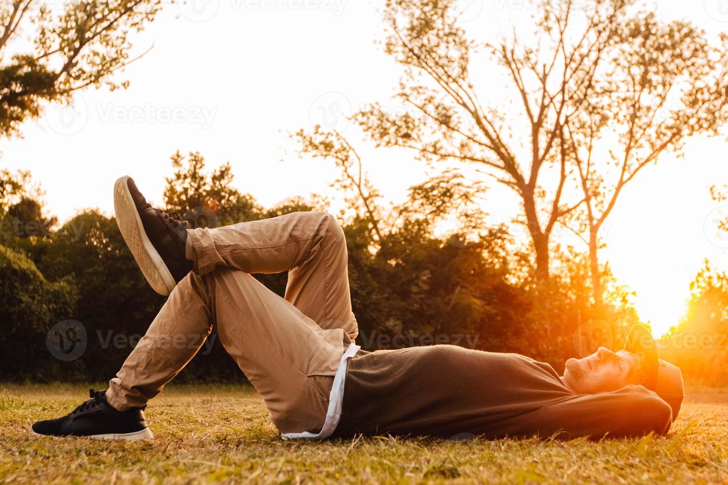 Hombre acostado sobre la hierba verde, disfrutando de una relajación al atardecer en un parque foto