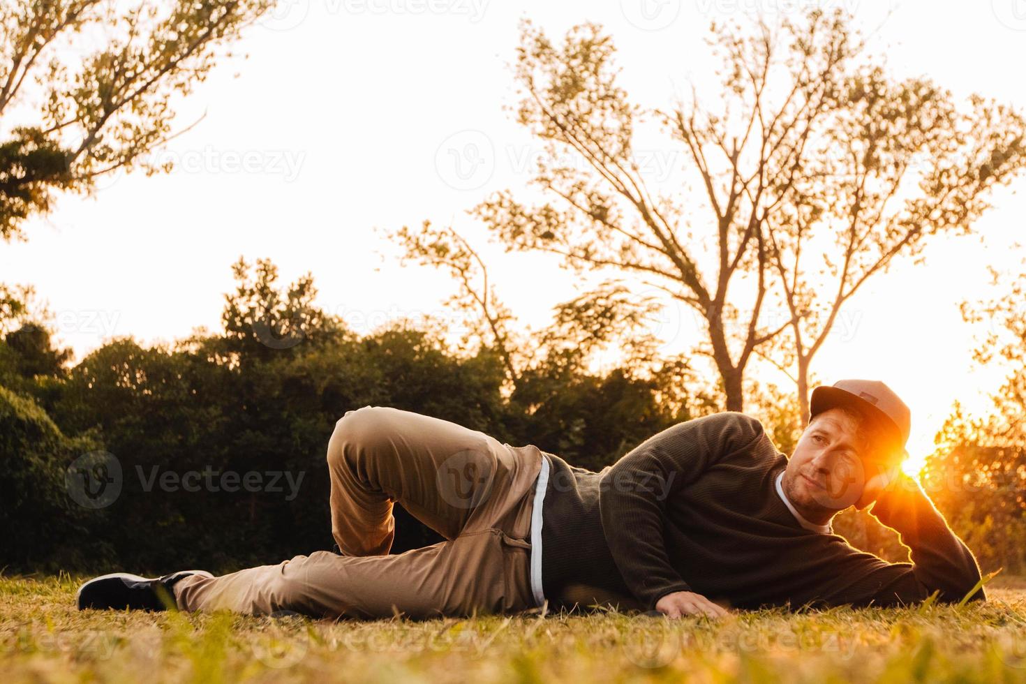 Hombre acostado sobre la hierba verde, disfrutando de una relajación al atardecer en un parque foto