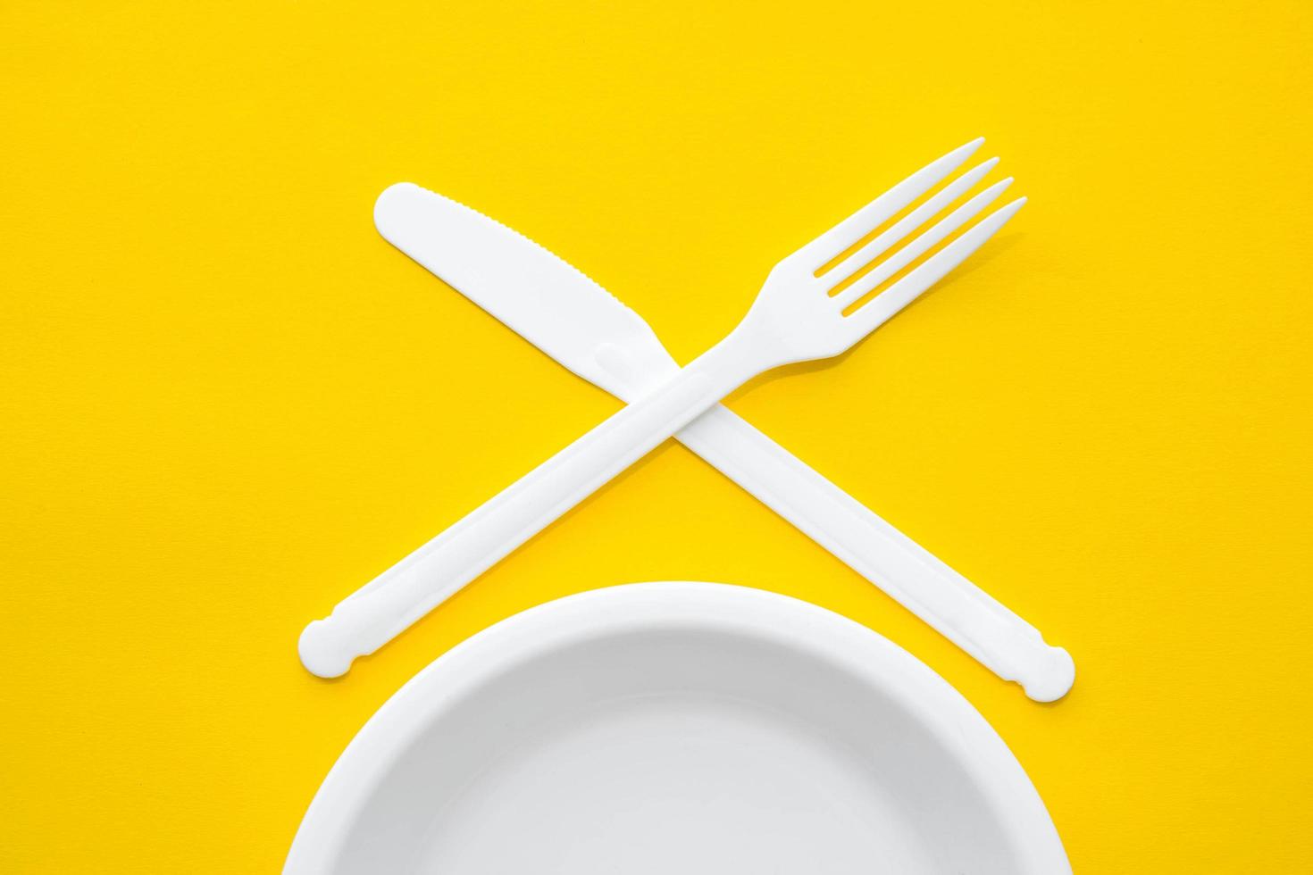 Plastic white fork, knife and plate on yellow background photo