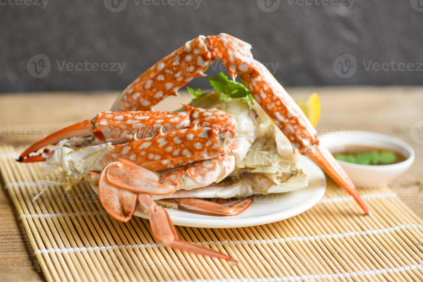 Carne de cangrejo - garras y patas de cangrejo cocidas en un plato blanco y salsa de mariscos en la mesa, cangrejo azul nadando foto