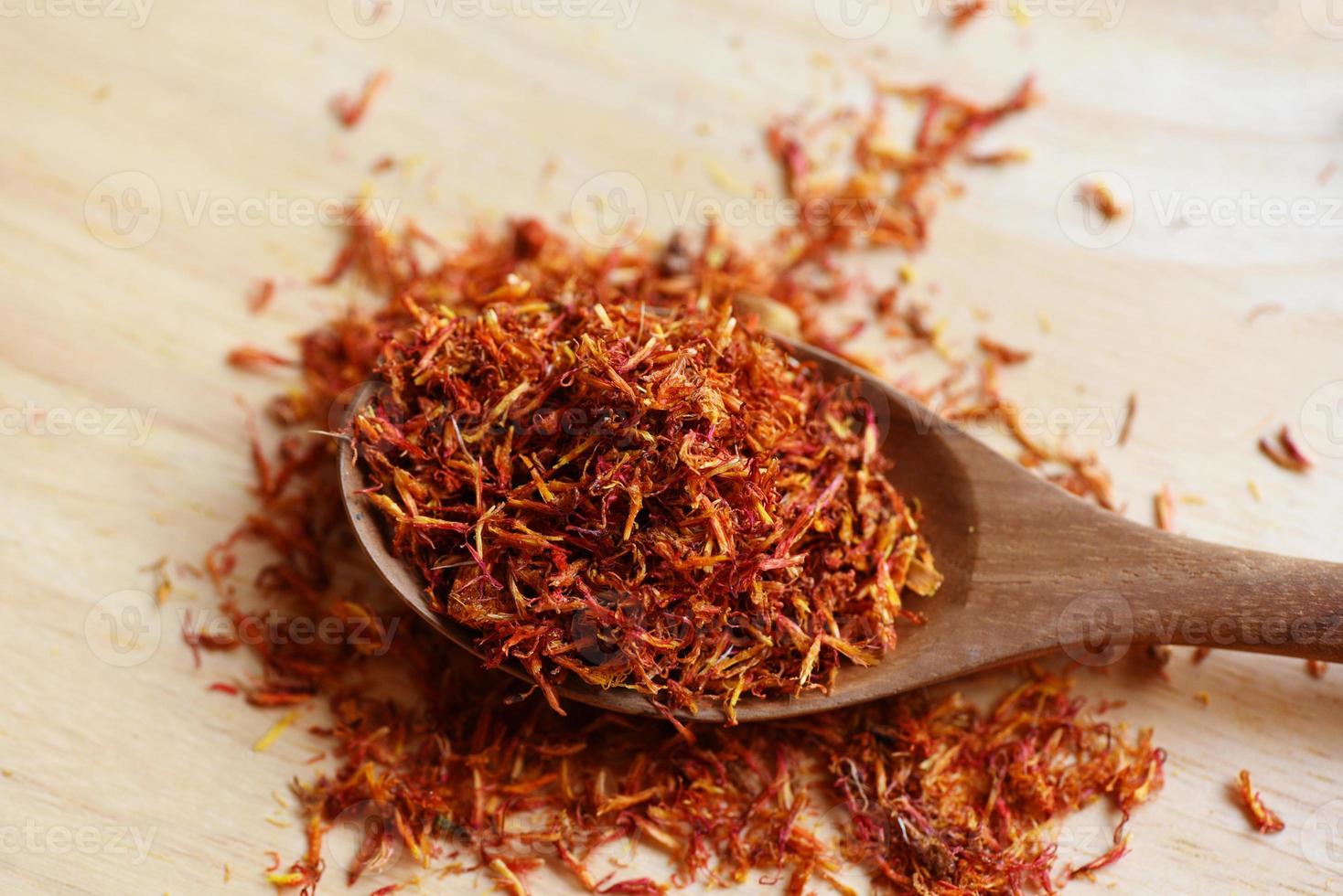 Dried safflower for herbal tea on wood background, dry safflower petals in wooden spoon, Saffron substitute photo