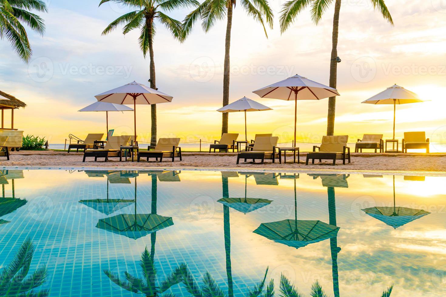 Umbrella and chair around swimming pool in hotel resort with sunrise in morning photo